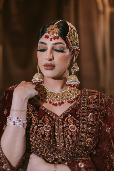 Gold-plated bridal jewelry set with red stone accents including choker necklace, jhumka earrings, tikka, and passa - South Asian bridal jewelry - Inaury