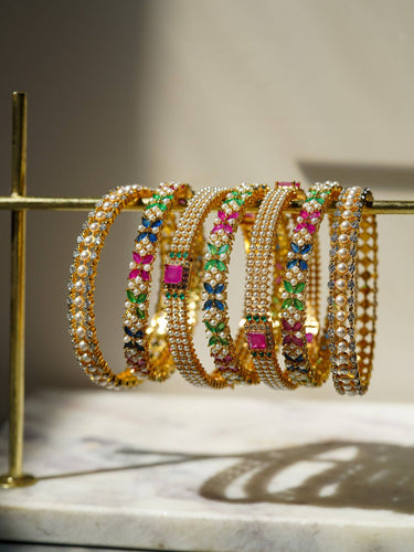 Anayasa 7-piece Gold Plated Bangle Set with colorful diamante accents, displayed on a gold stand for elegant jewelry presentation.