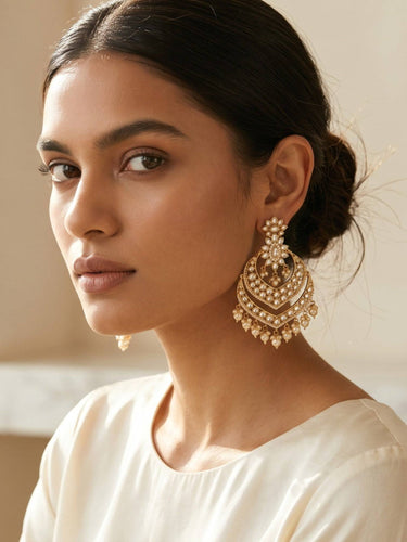 Woman wearing large, ornate gold Indian kundan earrings with a neutral background