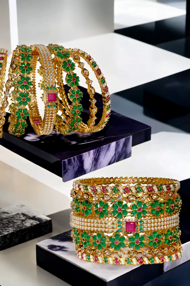 Arika gold-plated bangle set with floral emerald and ruby accents arranged on black and white marble. Ideal for festive and wedding attire.