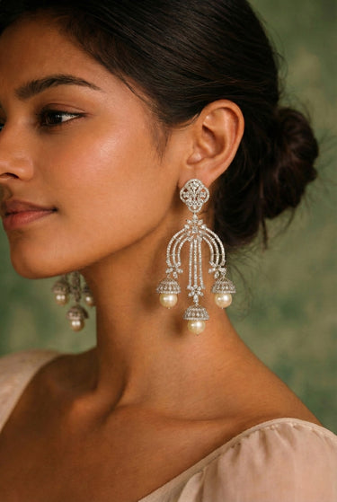 Woman wearing elegant silver earrings with pearls against a green background