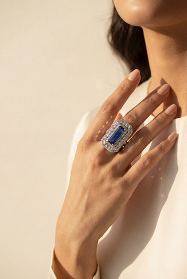 Hand wearing a ring with a blue gemstone on a neutral background from Inaury