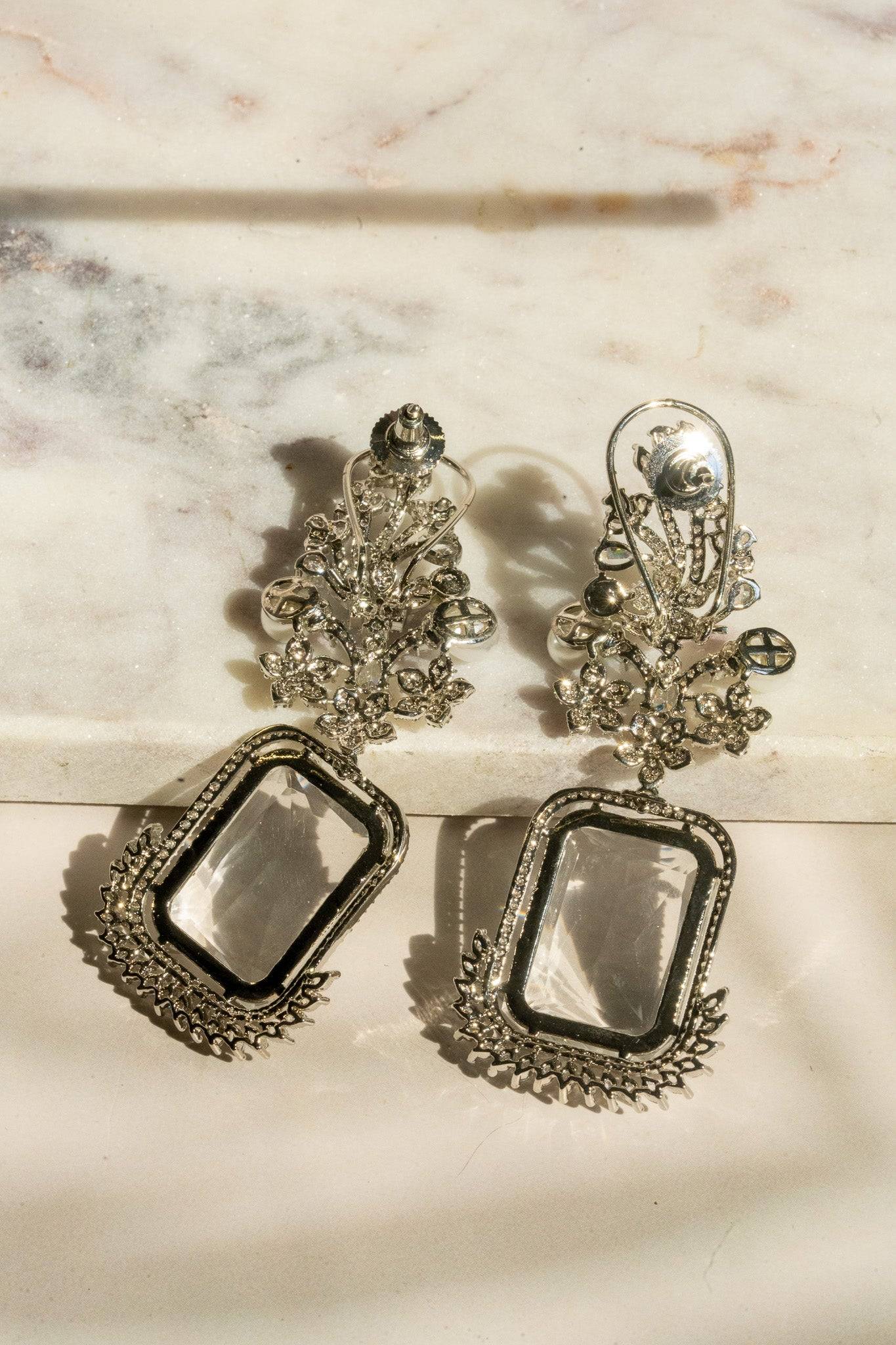 Back flat lay of Aayat Statement Earrings in crystal white with transparent gemstone and intricate rhodium-plated floral design.