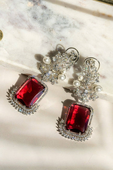 Flat lay of ruby red Aayat Statement Earrings with oversized gemstone, floral pavé setting, and pearl details. Elegant dangle earrings.