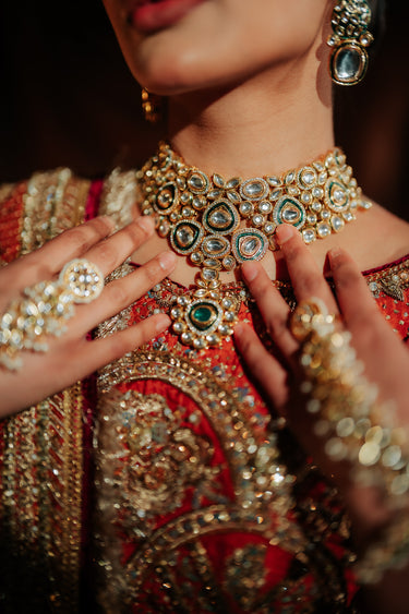 Close-up of a person wearing intricate jIndian bridal ewelry including a necklace, earrings, and bangles.