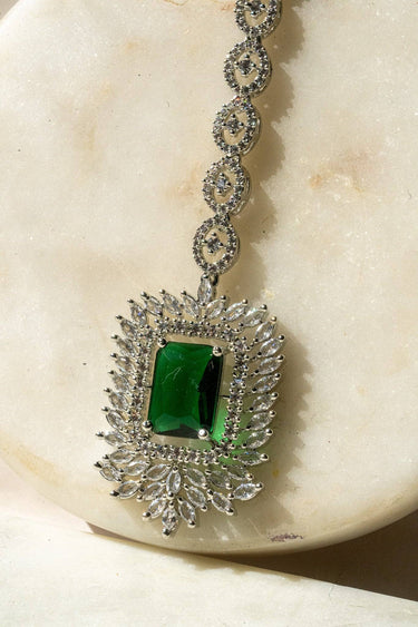 Angled view of Alora Maang Tikka in rhodium with green crystal centerpiece and sparkling AD accents.