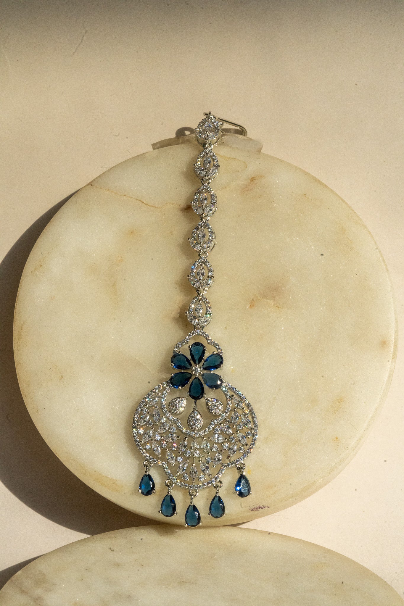 Rhodium-plated floral maang tikka with AD stones in a silver and sapphire blue from Inaury