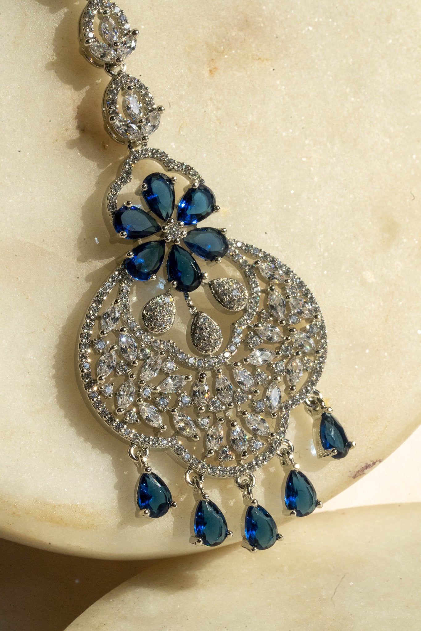 Rhodium-plated floral maang tikka with AD stones in a silver and sapphire blue from Inaury