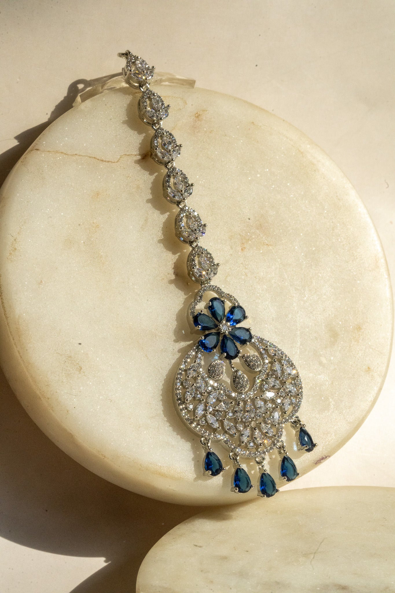 Rhodium-plated floral maang tikka with AD stones in a silver and sapphire blue from Inaury