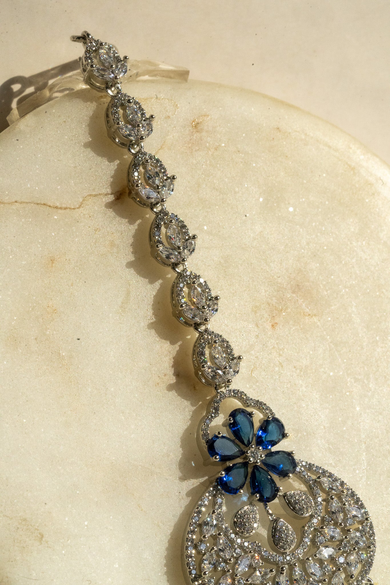 Rhodium-plated floral maang tikka with AD stones in a silver and sapphire blue from Inaury