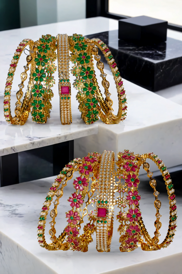 Arika 7-piece gold-plated bangle set featuring floral motifs with ruby and emerald stones. Perfect for bridal and traditional occasions.