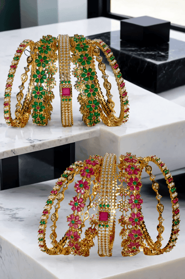 Arika 7-piece gold-plated bangle set featuring floral motifs with ruby and emerald stones. Perfect for bridal and traditional occasions.