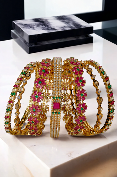 Close-up of Arika floral gold-plated bangles with ruby and emerald detailing. Premium jewelry set for celebrations and ethnic fashion.