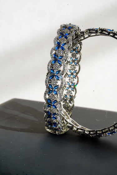 Macro close up of rhodium plated silver finish bangles with blue gemstones on a reflective surface