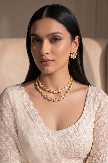 Model wearing gold plated Kundan double layer necklace set with matching stud earrings and an ivory embroidered outfit