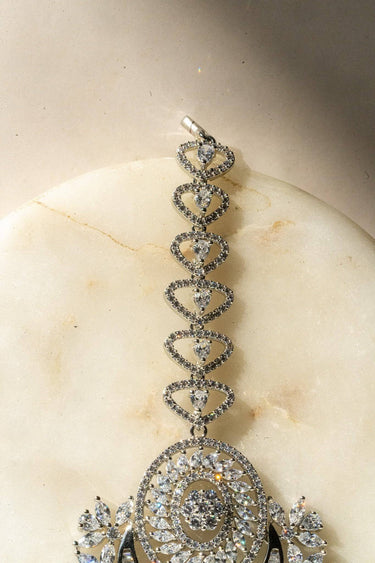 Iliyana Maang Tikka in rhodium finish with CZ stones, featuring a floral crescent design. Ideal for bridal and festive hair styling by Inaury.