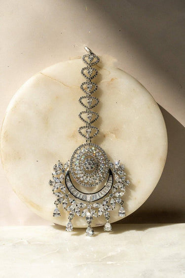 Iliyana Maang Tikka in rhodium finish with CZ stones, featuring a floral crescent design. Ideal for bridal and festive hair styling by Inaury.