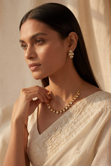 Side profile view of a model styling the delicate single-strand Dilara heart Kundan necklace over a white embroidered bridal saree.