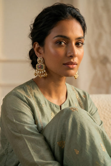 A front facing studio portrait of a model styling the gold plated Aadhya Kundan glass polki earrings with a sage green embroidered outfit.
