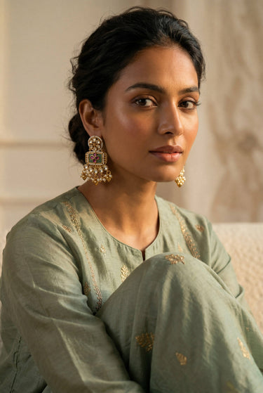 A front facing studio portrait of a model styling the gold plated Aadhya Kundan glass polki earrings with a sage green embroidered outfit.
