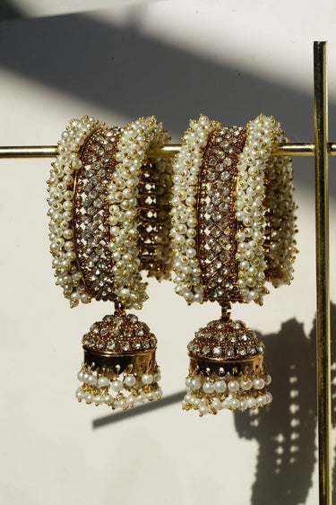 Macro close-up of the Aliya Jhumka Bangle in antique gold with faux pearl beadwork, focusing on the stacked bangle set with dangling jhumka charms.