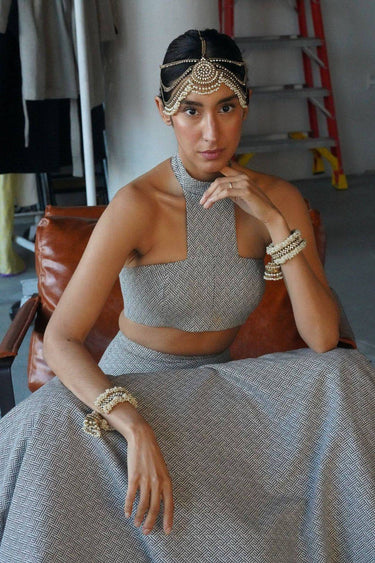 Close-up of the Aliya Jhumka Bangle Bracelet in antique gold with faux pearl beadwork, worn on a seated model in a grey contemporary South Asian outfit.