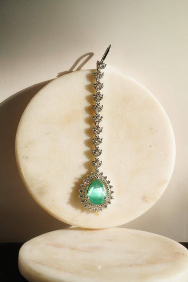 Close-up of green teardrop Amore AD Maang Tikka on marble coaster