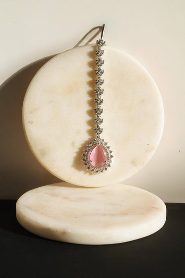 A close-up product view of the Amore rhodium-plated Maang Tikka headpiece featuring a light pink teardrop stone and crystal halo.
