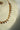 A side profile product view of the single-strand Dilara gold-plated necklace on a cream display bust, showcasing the continuous flow of clear heart stones.