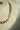 A side profile product view of the single-strand Dilara gold-plated necklace on a cream display bust, showcasing the continuous flow of clear heart stones.