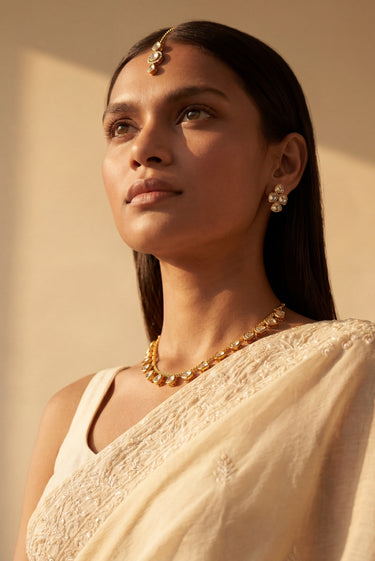 An upward editorial angle of a model showcasing the clear Dilara heart-cut Kundan strand necklace paired with matching studs and a delicate forehead maang tikka.