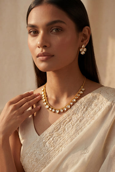 Front-facing portrait of a model wearing the Kiara minimalist gold-plated necklace with clear heart-cut glass Kundan stones and matching geometric cluster stud earrings.