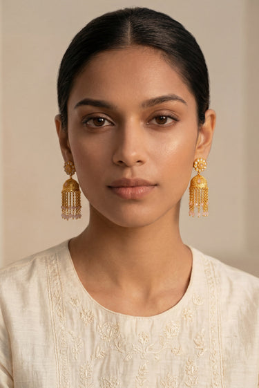 A clean front portrait of a model styling the gold plated Lara handcrafted filigree jhumka earrings paired with an elegant cream embroidered dress.