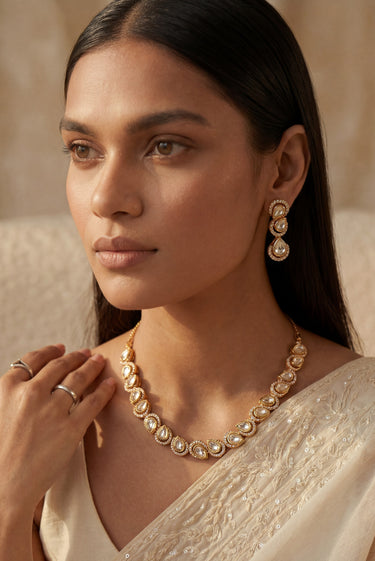 An elegant three-quarter lifestyle portrait of a model showcasing the gold-plated Mehr single-strand teardrop Moissanite necklace and matching cascading triple-tier drop earrings.