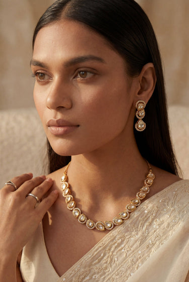An elegant three-quarter lifestyle portrait of a model showcasing the gold-plated Mehr single-strand teardrop Moissanite necklace and matching cascading triple-tier drop earrings.