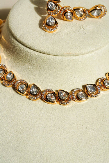 A premium studio presentation shot of the Mehr gold-plated necklace featuring a strand of teardrop Moissanite stones with halo borders resting on a cream display bust.