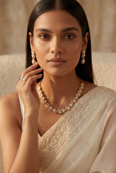 A front-facing lifestyle portrait of a model styling the complete Mehr gold-plated collection, featuring the teardrop Moissanite strand necklace, triple-tier drop earrings, and matching maang tikka.