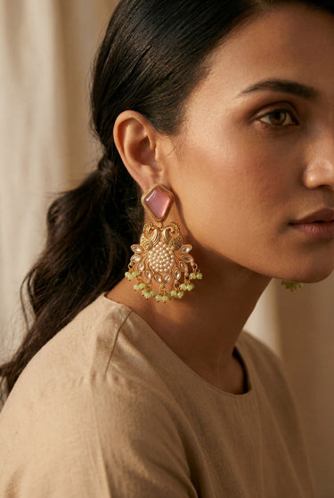 A macro profile shot of a model wearing the blush pink and mint green Mira peacock statement earrings to display the scale and fit against the jawline.