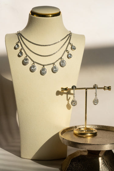 The complete Sania rhodium-plated minimalist Kundan necklace and hinged drop earring set displayed together on a white platform.
