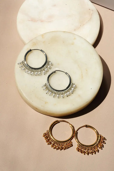 A full collection presentation showing both the gold ghungroo hoops and silver pearl hoops on a neutral surface.