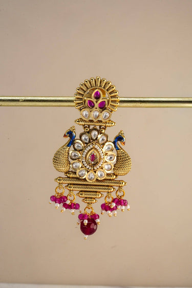 Inaury Adrita Kundan Meenakari Peacock Drop Earrings — single earring closeup showing sunburst stud with ruby Kundan stones, cobalt blue enamel peacocks, pearl-bordered lotus medallion and ruby bead pendant drop