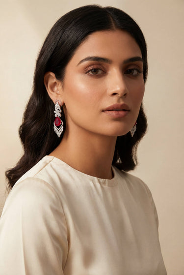 Inaury Nimisha AD Drop Earrings in Ruby on model — rhodium-plated chandelier earrings with ruby-red teardrop center stone and AD floral cluster