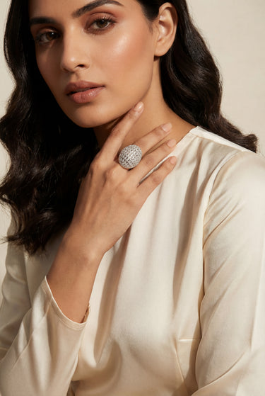 Woman wearing a large diamond ring on her finger against a neutral background