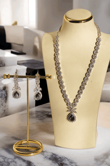 Lina Long Diamante Accent AD Necklace Set - Rhodium-plated with white AD stones, featuring intricate patterns and pendant-like centerpiece, available in silver & sapphire blue, silver & purple, and silver & citrine yellow, with matching dangling earrings.