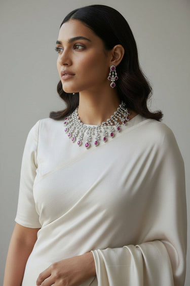 Angled view of Raha Diamante classic necklace and chandelier earrings with ruby pink accents on white saree