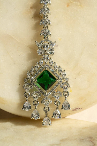 Rhodium-plated maang tikka with an emerald green center and teardrop-shaped white AD stones from Inaury