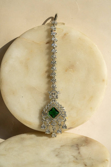 Rhodium-plated maang tikka with an emerald green center and teardrop-shaped white AD stones from Inaury