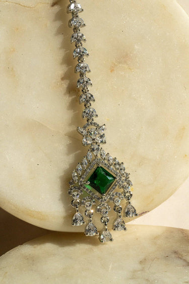 Rhodium-plated maang tikka with an emerald green center and teardrop-shaped white AD stones from Inaury