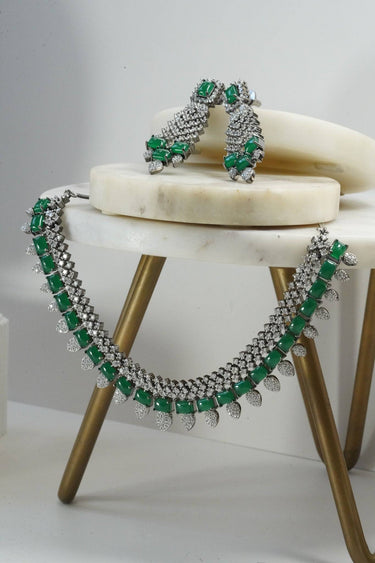 Green variant of Anjam Black Plated AD Necklace Set with dazzling AD stones and matching earrings, styled on a marble and brass stand.