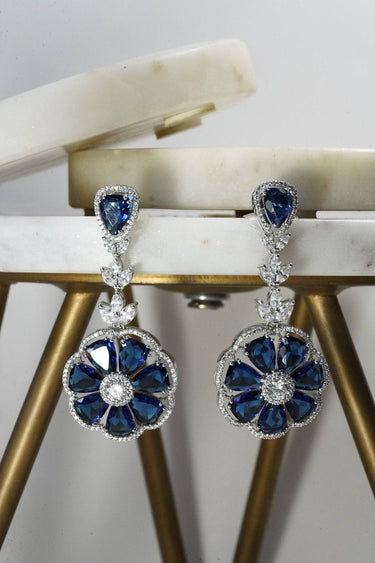 Detailed view of Chahat Floral AD earrings in sapphire blue. Rhodium-plated with floral-cut stones and teardrop tops.